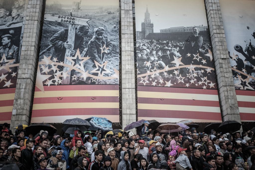 Under large photos of Soviet military scenes from World War II, spectators watch the parade.